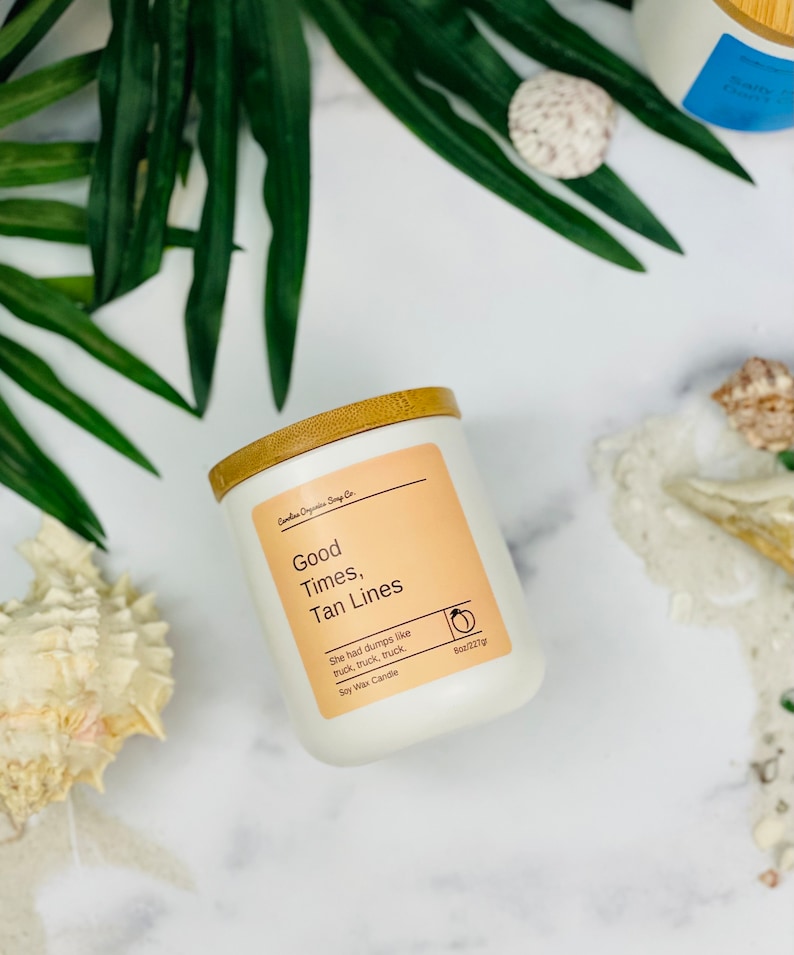 Puede incluir: Vela de cera de soja blanca con tapa de bamb&uacute;. La etiqueta dice "Good Times, Tan Lines" y "She had dumps like truck, truck, truck". La vela es de 8 oz/227g.