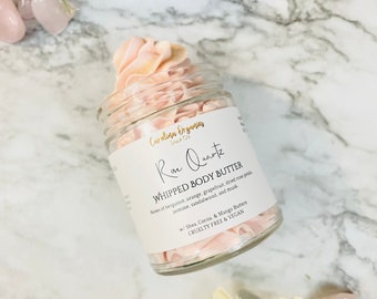 May include: A glass jar of pink whipped body butter with the label "Rae Quartz Whipped Body Butter" and the ingredients listed below. The label also states "Cruelty Free & Vegan".