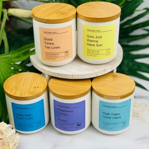 Puede incluir: Seis velas de cera de soja con tapas de madera y etiquetas coloridas. Las etiquetas presentan frases con tem&aacute;tica veraniega como "Good Times, Tan Lines", "Girls Just Wanna Have Sun", "Salty Hair, Don't Care", "Happiness Comes In Waves", y "High Tides, Good Vibes".