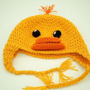 May include: A yellow crocheted hat with a duck face. The hat has orange beak and black eyes. The hat has a long yellow crocheted tie.