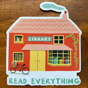 May include: A red brick building with a sign that says "LIBRARY" and a bicycle with a basket full of books in front of it. The building has a pink roof and a green vine growing up the side. The text "READ EVERYTHING" is written below the building.