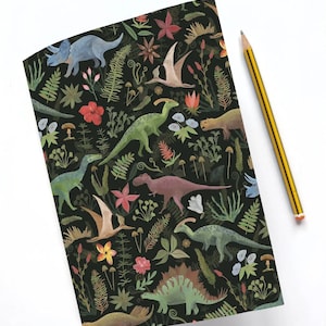 Puede incluir: Un cuaderno con fondo negro que presenta un colorido patrón de dinosaurios y plantas. Un lápiz a rayas amarillas y negras descansa sobre la superficie blanca junto al cuaderno. El diseño del cuaderno incluye varios dinosaurios, flores y helechos.