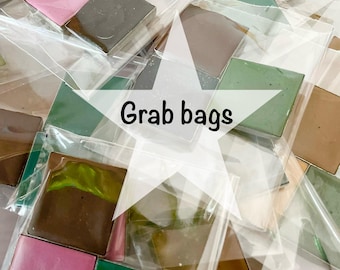 May include: Multiple clear plastic bags containing assorted square-shaped solid paint pans in various colors including pink, green, brown, yellow, and grey. A white star-shaped graphic overlay in the center displays the black text Grab bags.