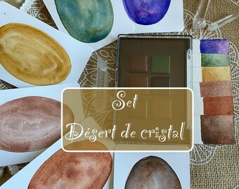 May include: A watercolor art set featuring oval-shaped color swatches in various hues, including blue, gold, and brown. A palette of earth-toned paints and a color chart are also visible. The text "Set Désert de cristal" is displayed.