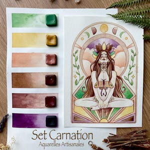 Peut inclure: Un ensemble de peinture aquarelle avec six godets de pigments carrés, une feuille de papier avec des échantillons de couleurs et une illustration détaillée d'une figure en position du lotus. Le texte indique Set Carnation Aquarelles Artisanales Le Cattelier.