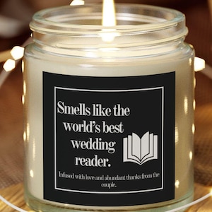 May include: A white candle with a black label that reads "Smells like the world's best wedding reader.  Infused with love and abundant thanks from the couple." The candle is sitting on a wooden coaster and surrounded by white fairy lights.