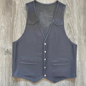 May include: A black leather vest with a V-neck and a button closure. The vest has two pockets on the front and a pointed hem.