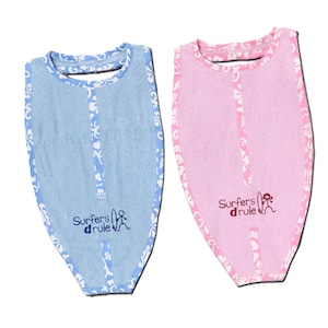 Puede incluir: Dos baberos de rizo para bebé con un diseño de surfista. Un babero es azul con ribete blanco y el otro es rosa con ribete blanco. Ambos baberos tienen el texto "Surfers d'rule" y un gráfico de surfista.