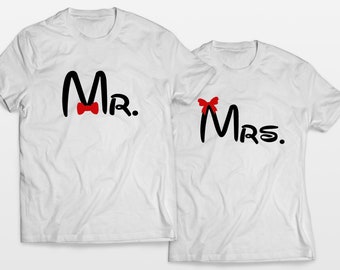 Puede incluir: Dos camisetas blancas con texto negro y lazos rojos. La camiseta de la izquierda dice "Mr." con una corbata de lazo. La camiseta de la derecha dice "Mrs." con un lazo.