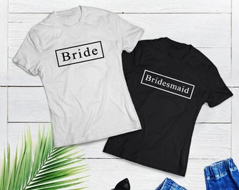 Puede incluir: Dos camisetas, una blanca y otra negra, con las palabras "Bride" y "Bridesmaid" impresas en ellas en un cuadro negro.