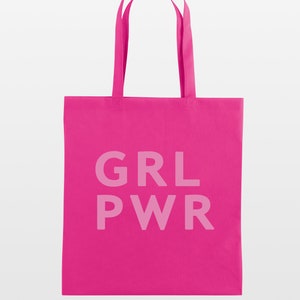 May include: A bright pink tote bag with the text "GRL PWR" printed in a lighter pink. The bag has two matching pink handles for carrying. The bag is made of a solid color fabric.