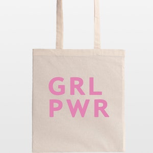 May include: A beige tote bag with the pink text "GRL PWR" printed on the front. The bag has two beige handles and is made of a canvas-like material. The bag is designed for carrying items.
