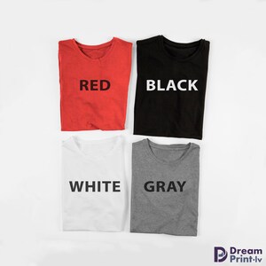 May include: Four folded t-shirts in different colors: red, black, white, and gray. Each shirt has the color name printed on the front in white.