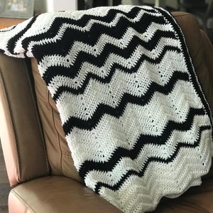 May include: Black and white chevron crochet throw blanket draped over a brown leather armchair.