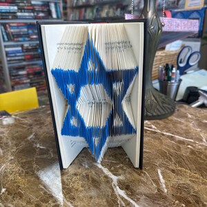 May include: A blue and white paper star of David, folded from the pages of a book, stands on a brown marble surface.