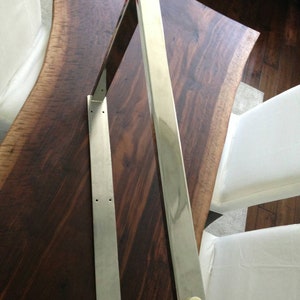May include: A silver metal shelf bracket with two white plastic caps on the ends. The bracket is mounted on a dark wood surface.