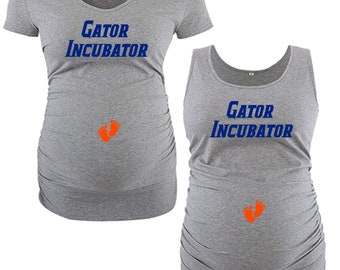 May include: Two gray maternity shirts with the text "Gator Incubator" in blue and a pair of orange footprints. One shirt is a short-sleeved t-shirt and the other is a tank top.