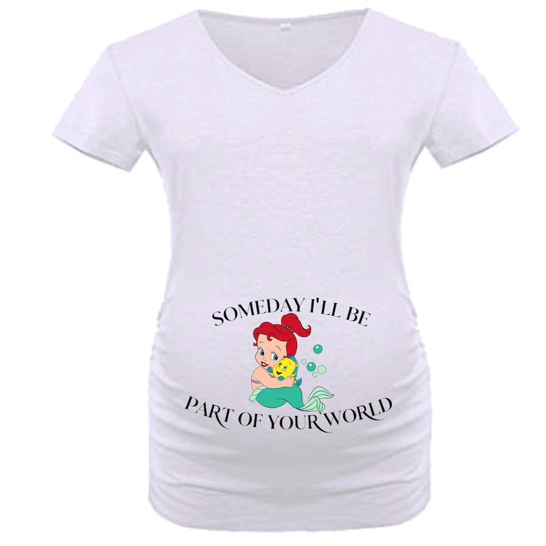 Op de afbeelding: Witte zwangerschaps-t-shirt met een V-hals. De shirt heeft een afbeelding van Ariel uit De Kleine Zeemeermin die Botje omhelst, met de tekst "Someday I'll be part of your world" in zwart.