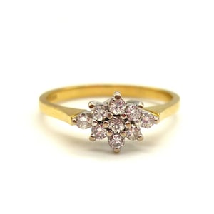 May include: A gold ring featuring a cluster of small, round, clear gemstones arranged in a floral pattern. The ring has a thin, gold band and a white metal setting for the gemstones.