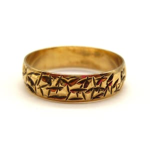 Peut inclure: Une bague dorée avec un motif détaillé de formes gravées en forme de feuilles. La bague a un intérieur lisse et poli et un extérieur texturé. La bague est de style alliance, et le motif enveloppe toute la circonférence.