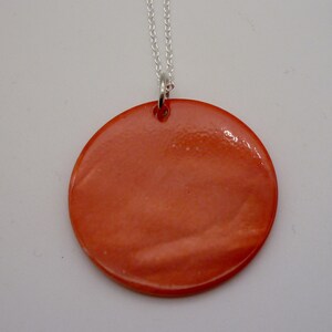 May include: A silver chain necklace with a large, round, orange pendant. The pendant is made of a smooth, shiny material.