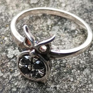 May include: A silver ring featuring a black gemstone set in a stylised owl design.