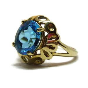 May include: A gold ring with a large, oval-shaped blue gemstone set in a delicate, ornate design.