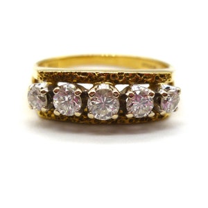 以下が含まれることがあります： 5つの丸いダイヤモンドが1列に並んだゴールドのバンドリング。バンドはテクスチャ加工が施され、わずかに盛り上がった縁があります。