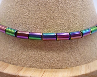 Op de afbeelding: Een close-up van een veelkleurige kralenketting. De kralen zijn klein en cilindrisch, met een metallic afwerking. De kleuren van de kralen zijn iriserend, met tinten groen, blauw, paars en roze.