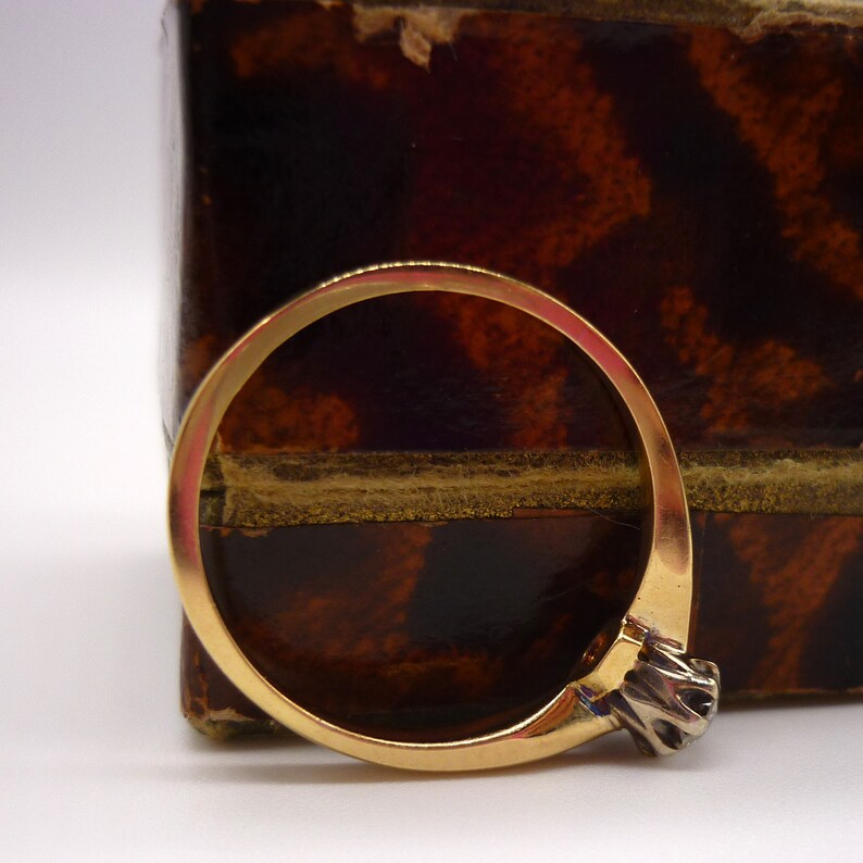 May include: A gold band ring with a single, clear, round gemstone set in a silver prong setting.