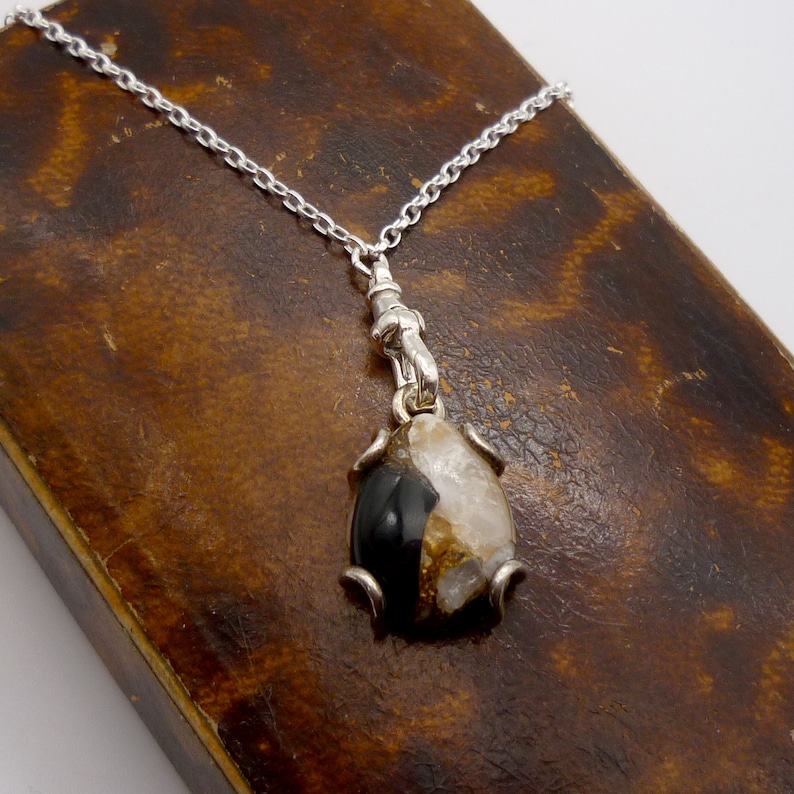 May include: A silver chain necklace with a pendant featuring a black and white agate stone set in a silver frame.