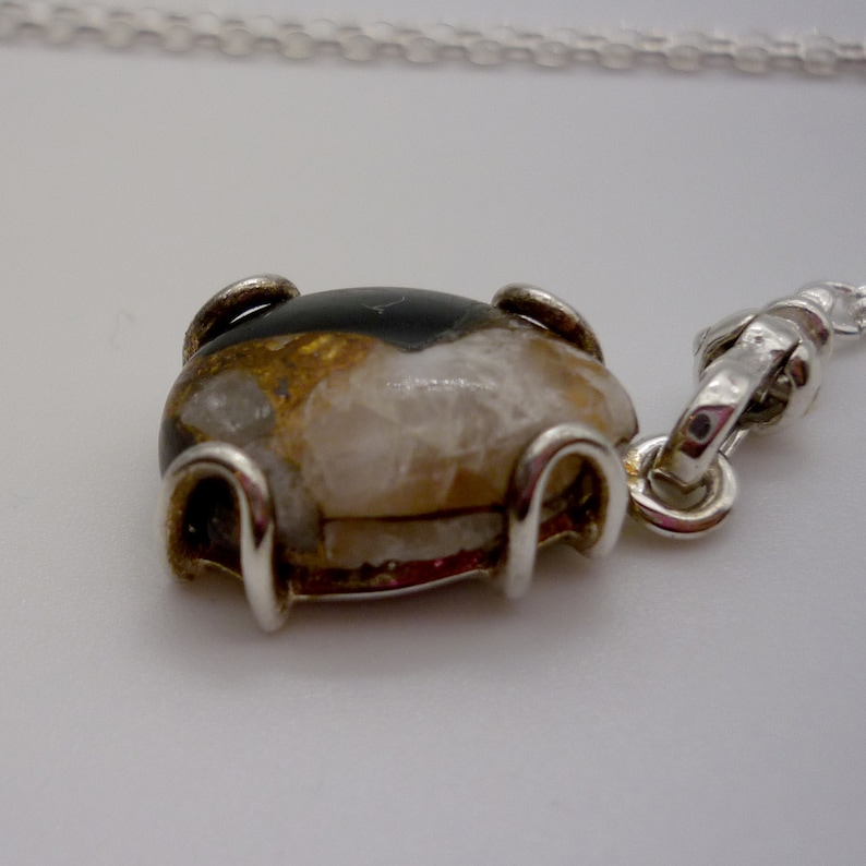 May include: A silver chain necklace with a pendant featuring a brown, white, and black stone set in a silver bezel.