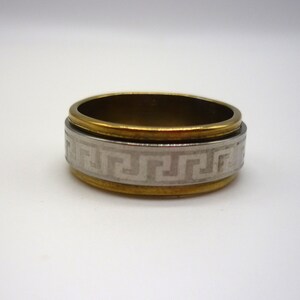 May include: A gold and silver ring with a Greek key design. The ring is made of metal and has a smooth finish.