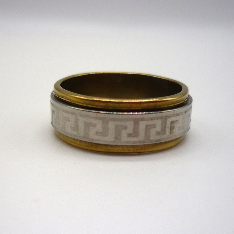 May include: A gold and silver ring with a Greek key design. The ring is made of metal and has a smooth finish.