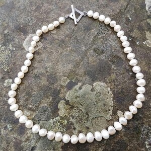 May include: A white pearl necklace with a silver clasp. The necklace is made of small, round pearls and is approximately 46 cm long.