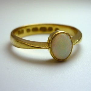 May include: A gold ring with a white opal gemstone. The ring has a simple band and the opal is set in a bezel setting.