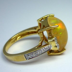 May include: A gold ring with a large, round, yellow opal gemstone set in a prong setting. The ring has a band of small diamonds set in a pave setting.