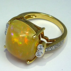 May include: A gold ring with a large, yellow opal gemstone set in a prong setting. The ring band is decorated with a row of small diamonds.
