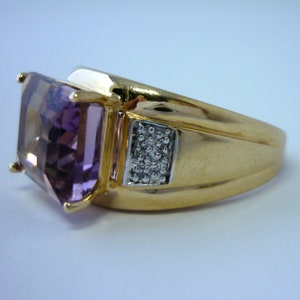 May include: A gold ring featuring a large, square-cut amethyst gemstone and a smaller square-cut diamond accent. The ring has a thick band.