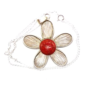 May include: A silver flower pendant necklace with a red coral centre. The pendant is detailed with a textured, striated design.