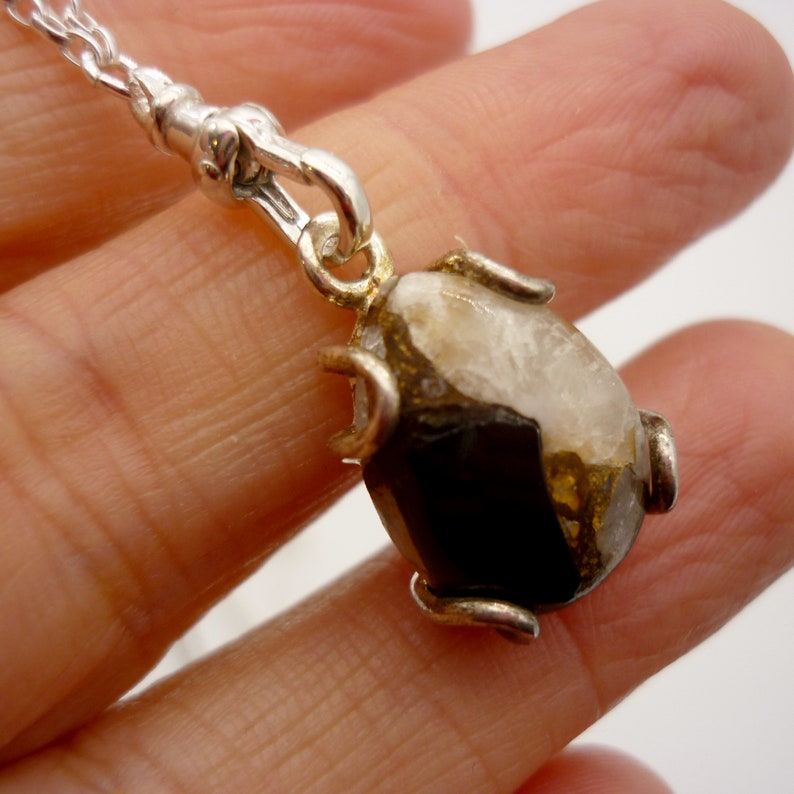 May include: A silver chain necklace with a pendant featuring a brown and white gemstone set in a silver frame.