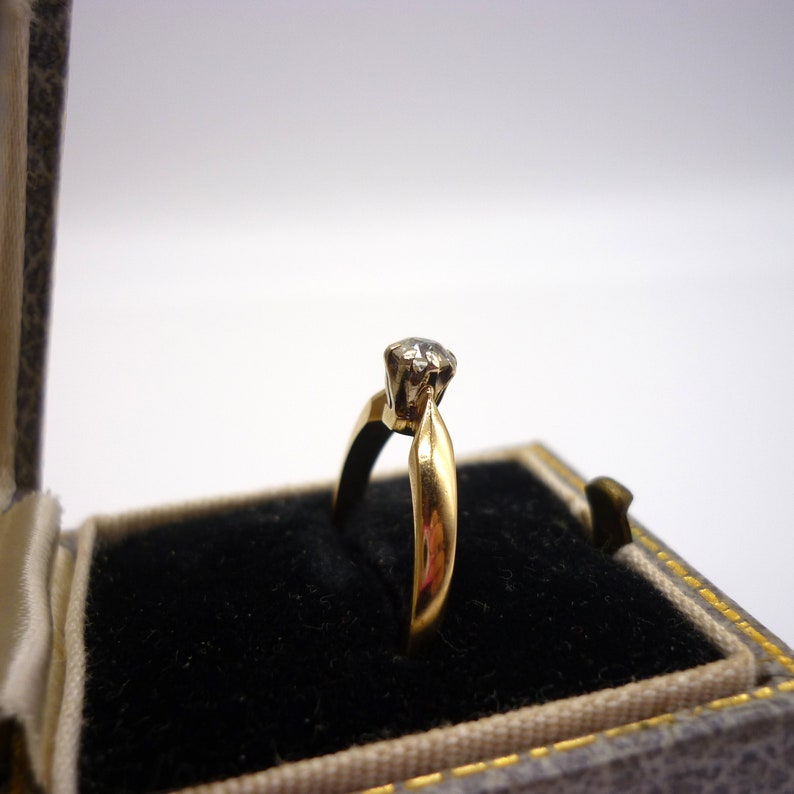 May include: A gold engagement ring with a single round diamond in a black velvet ring box.