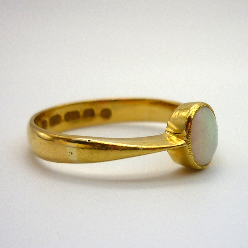 May include: A gold ring with a white opal gemstone. The ring is simple and elegant, with a smooth band and a round stone.