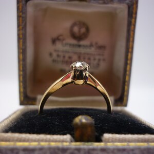May include: A gold ring with a single round diamond in a classic setting. The ring is in a small velvet-lined box.