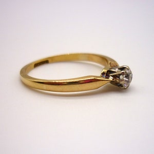 May include: A gold band engagement ring with a single round diamond set in a prong setting.
