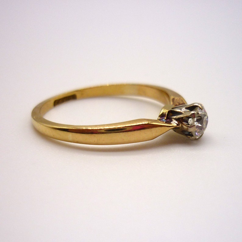 May include: A gold band engagement ring with a single round diamond set in a prong setting.