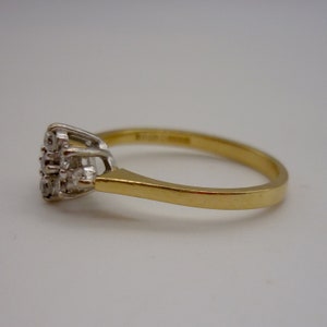 May include: A gold ring with a cluster of small, clear gemstones. The ring has a simple, elegant design with a gold band and a white metal setting for the gemstones. The gemstones are arranged in a floral or starburst pattern.