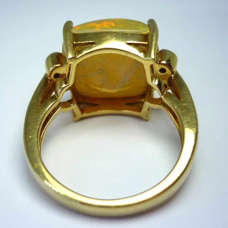 May include: A gold ring with a large, rectangular, opal gemstone set in a bezel setting. The ring has a simple, elegant design.