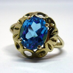 May include: A gold ring with a large, oval-shaped blue topaz gemstone set in a delicate, ornate setting.