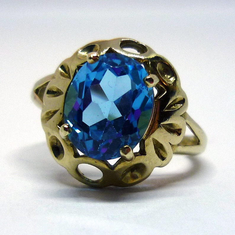 May include: A gold ring with a large, oval-shaped blue topaz gemstone set in a delicate, ornate setting.